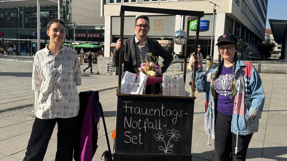 3 Personen in der Fußgänger*innenzone mit einem dekorierten Handwagen.